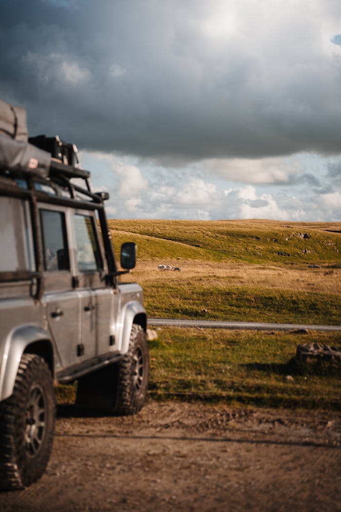 A 4x4 vehicle explores the vast open grasslands under a dramatic cloudy sky.