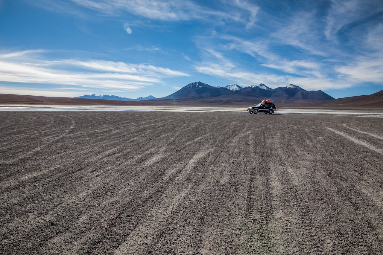 Services Expansive desert landscape in Uyuni, Bolivia, featuring a single SUV against distant mountains and a wide, clear sky.